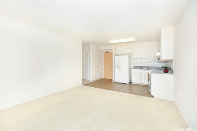 interior space with tasteful backsplash, light countertops, white cabinetry, a sink, and white fridge with ice dispenser