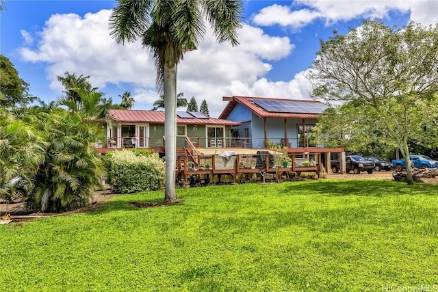 rear view of property featuring solar panels, metal roof, a standing seam roof, a yard, and a wooden deck