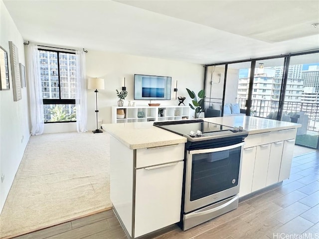 kitchen with a kitchen island, wood finish floors, stainless steel electric stove, white cabinetry, and open floor plan