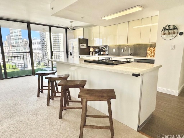 kitchen with stainless steel fridge with ice dispenser, floor to ceiling windows, light countertops, decorative backsplash, and a kitchen breakfast bar