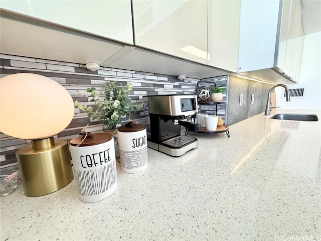 interior details with white cabinets, light stone countertops, and a sink