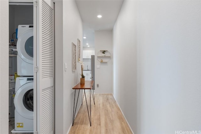 washroom featuring recessed lighting, stacked washer / dryer, light wood-type flooring, laundry area, and baseboards