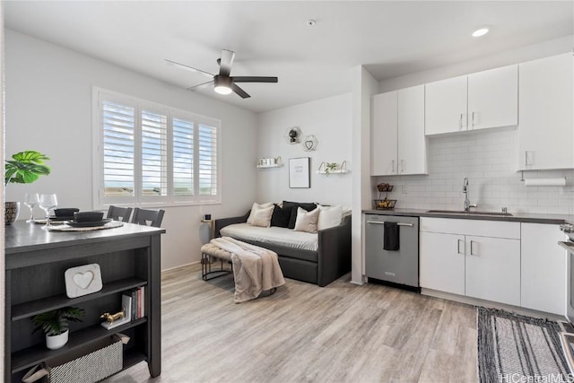 kitchen featuring a sink, stainless steel dishwasher, backsplash, light wood finished floors, and dark countertops