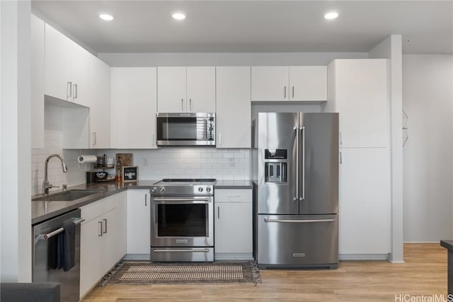 kitchen featuring appliances with stainless steel finishes, dark countertops, a sink, and light wood-style flooring