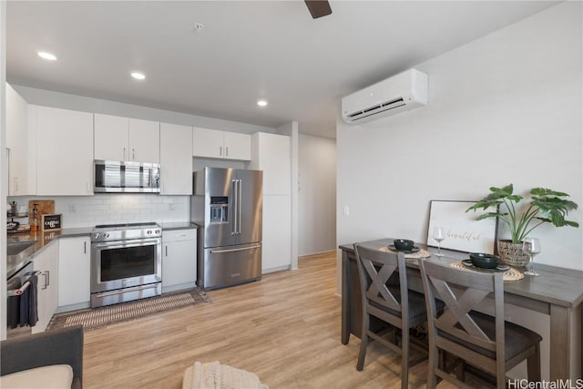 kitchen with light wood-style flooring, white cabinetry, an AC wall unit, appliances with stainless steel finishes, and decorative backsplash