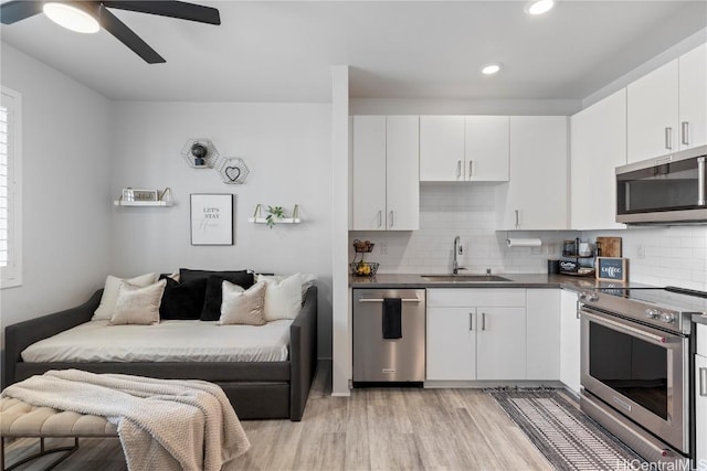 kitchen featuring dark countertops, appliances with stainless steel finishes, white cabinetry, a sink, and light wood-type flooring