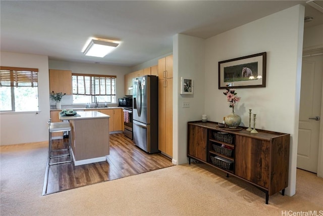 kitchen with appliances with stainless steel finishes, light colored carpet, light brown cabinets, and a sink