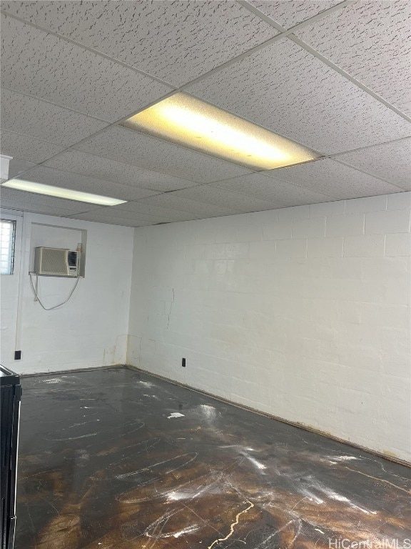 spare room with concrete block wall, a wall unit AC, and a paneled ceiling