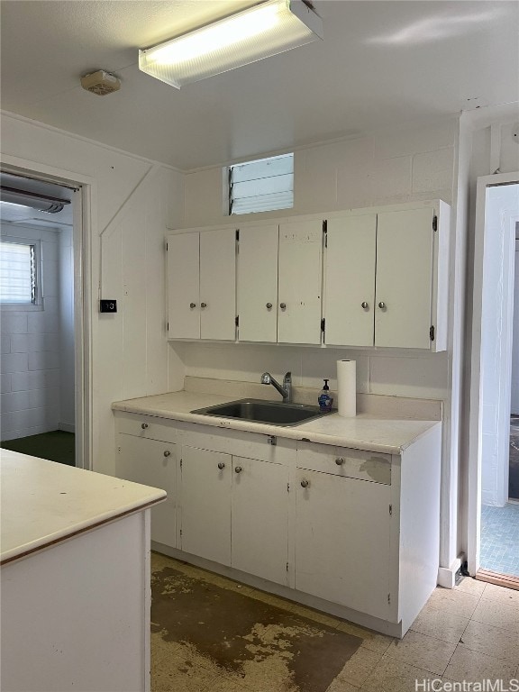 kitchen featuring light countertops, white cabinets, a sink, and unfinished concrete flooring