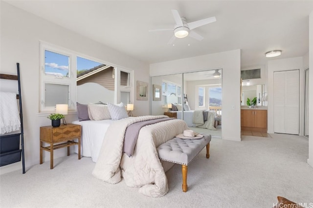 bedroom featuring ensuite bathroom, a closet, a ceiling fan, and light colored carpet