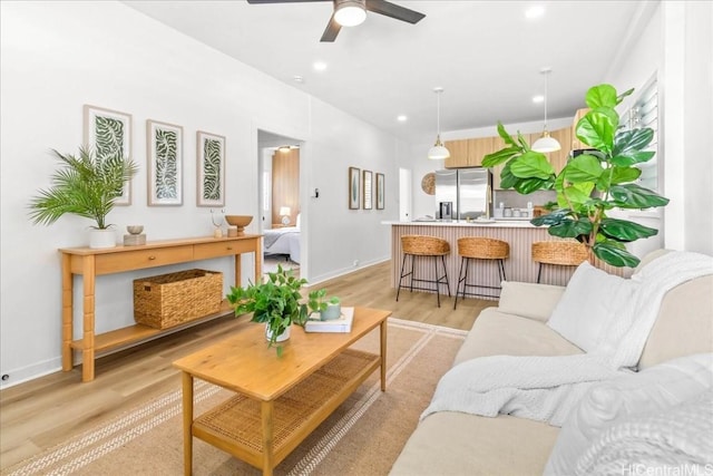 living room featuring light wood-type flooring, baseboards, and a ceiling fan