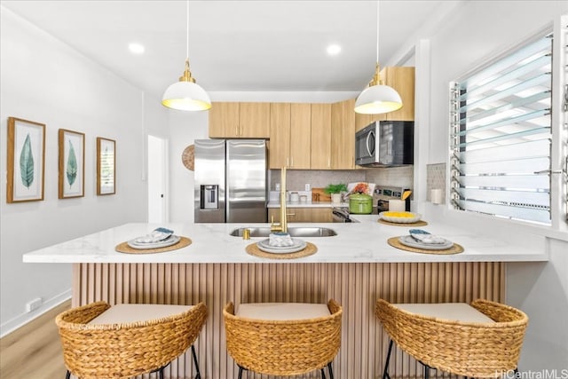 kitchen featuring appliances with stainless steel finishes, a peninsula, a sink, hanging light fixtures, and backsplash