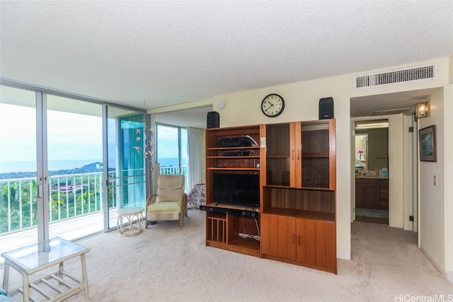 unfurnished living room featuring light carpet, a textured ceiling, a wall of windows, and visible vents