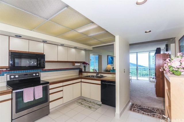kitchen with light tile patterned floors, backsplash, white cabinets, a sink, and black appliances