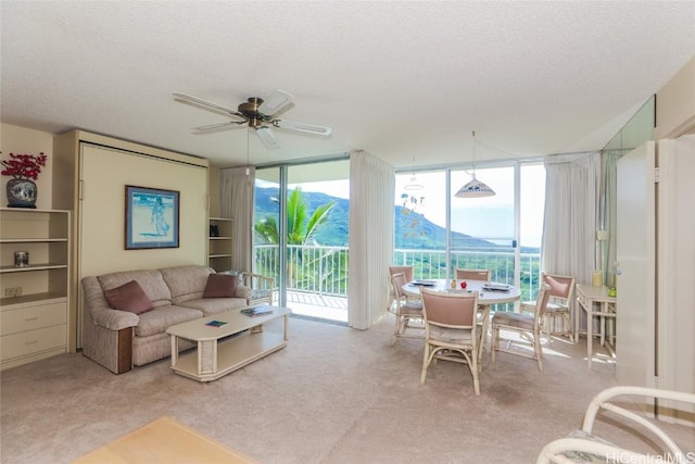 living room with a ceiling fan, a wall of windows, a textured ceiling, carpet flooring, and a mountain view