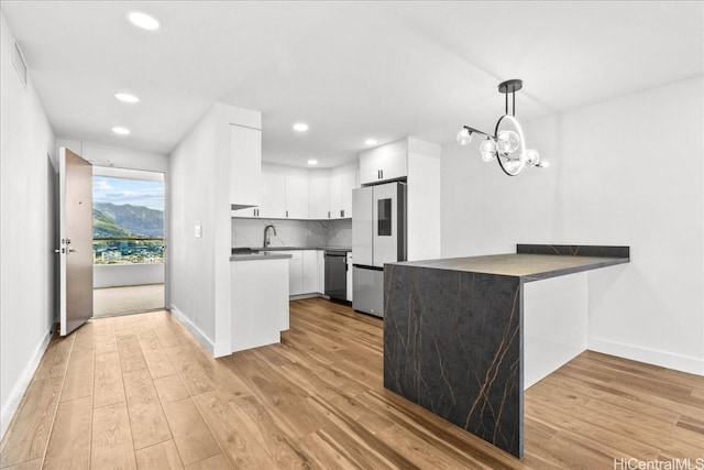 kitchen with a peninsula, white cabinetry, freestanding refrigerator, decorative backsplash, and dishwasher