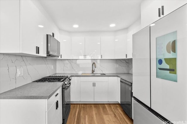 kitchen with a sink, white cabinets, light wood-type flooring, backsplash, and black range with gas stovetop