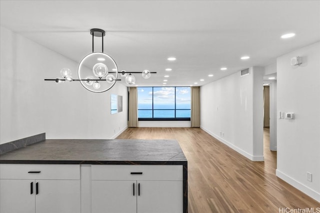 kitchen featuring a peninsula, wood finished floors, visible vents, white cabinetry, and dark countertops