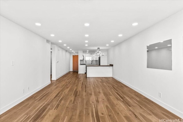 unfurnished living room featuring baseboards, recessed lighting, wood finished floors, and a notable chandelier