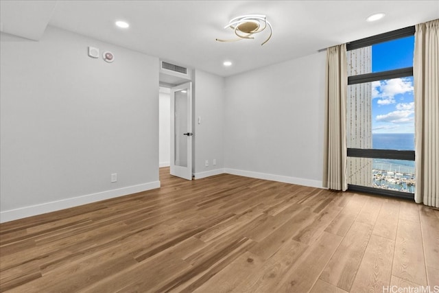 empty room with a wall of windows, wood finished floors, visible vents, and baseboards