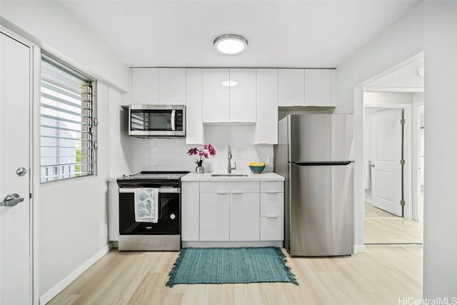 kitchen featuring light wood-style flooring, stainless steel appliances, a sink, white cabinetry, and backsplash