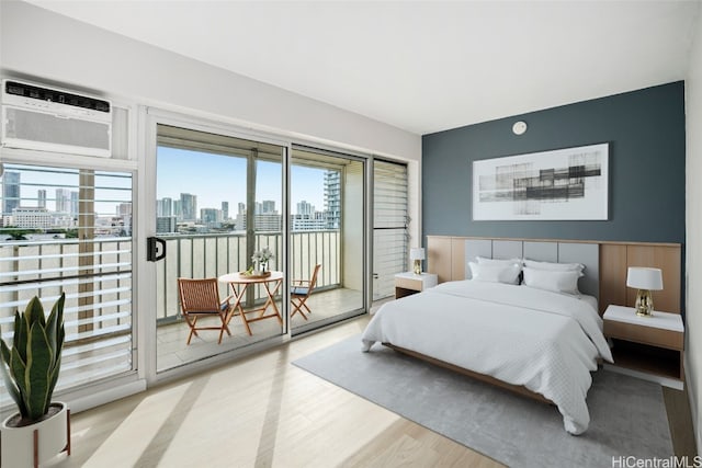 bedroom with light wood-style floors, a view of city, access to outside, and an AC wall unit