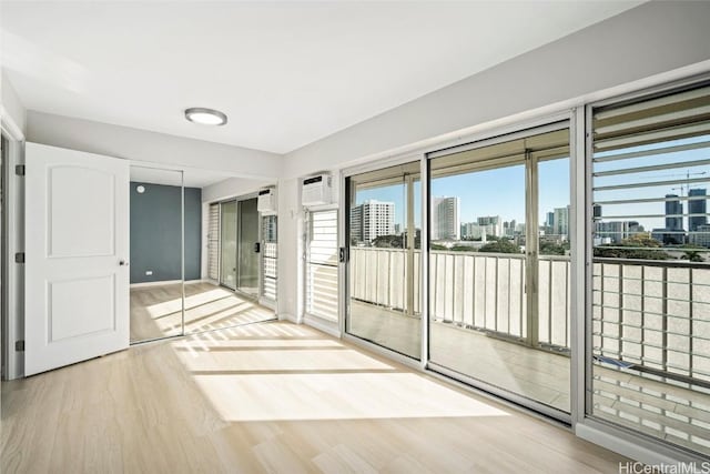 empty room featuring a view of city, a wall unit AC, wood finished floors, and baseboards