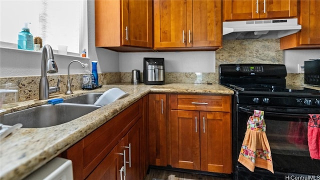 kitchen with light stone counters, under cabinet range hood, a sink, black appliances, and brown cabinetry