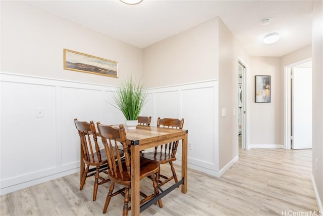 dining space with light wood finished floors, wainscoting, and a decorative wall