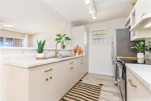 kitchen with light wood-style floors, white cabinets, a sink, track lighting, and range with electric cooktop