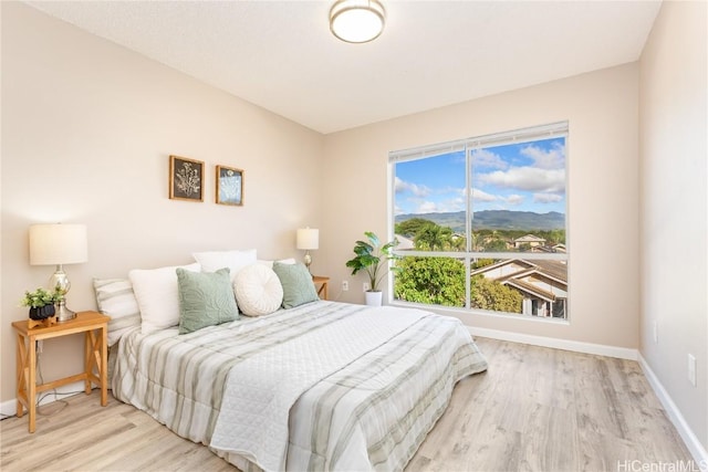 bedroom with light wood finished floors, baseboards, and a mountain view