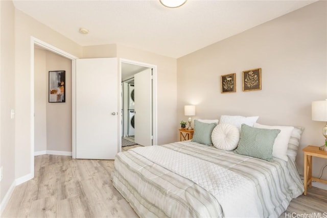 bedroom with baseboards, light wood-type flooring, and stacked washer / drying machine