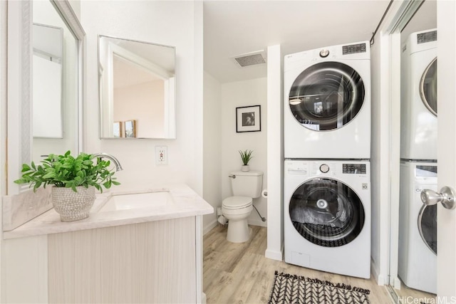 laundry room with stacked washer / drying machine, visible vents, light wood-style flooring, a sink, and laundry area