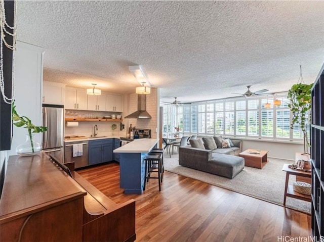 kitchen featuring a breakfast bar area, a sink, light countertops, appliances with stainless steel finishes, and wall chimney exhaust hood