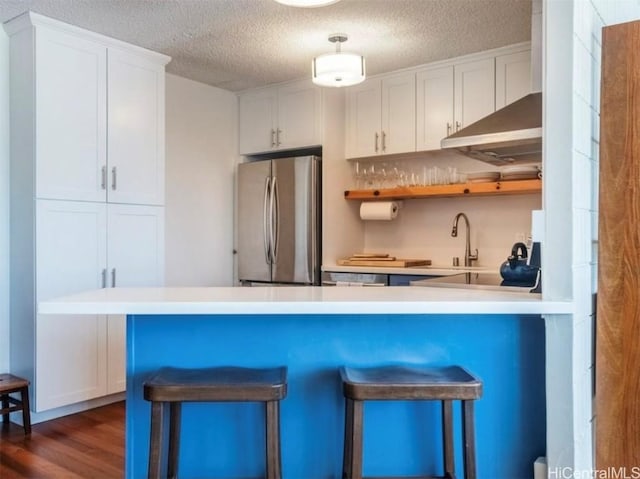 kitchen featuring a breakfast bar, dark wood-style flooring, freestanding refrigerator, white cabinets, and a sink