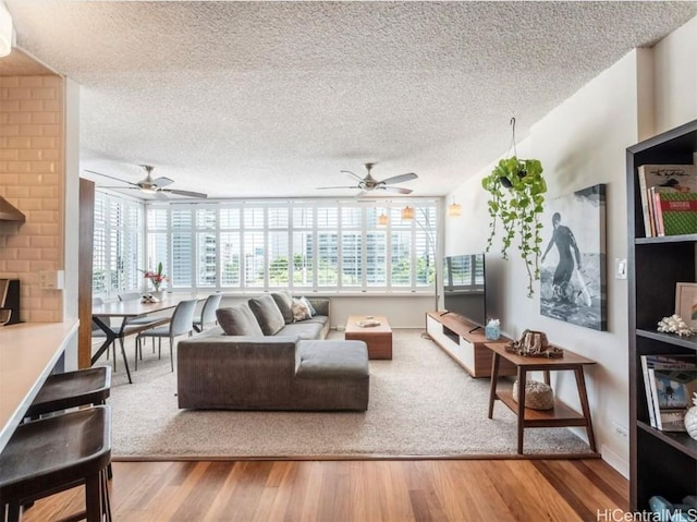 living area featuring a textured ceiling, ceiling fan, wood finished floors, and a healthy amount of sunlight