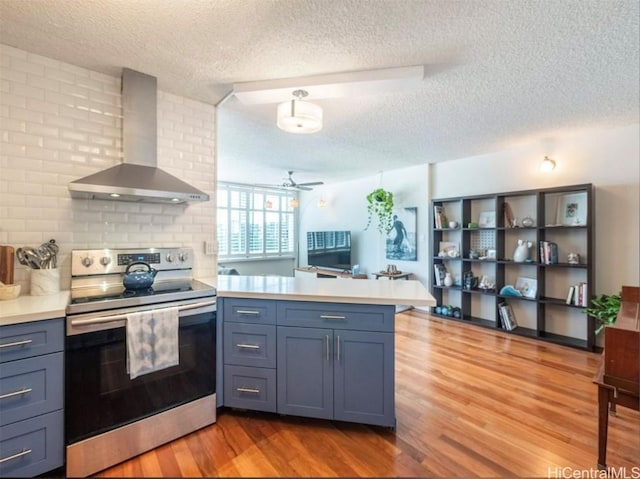 kitchen with electric stove, light countertops, light wood-style flooring, wall chimney range hood, and a peninsula