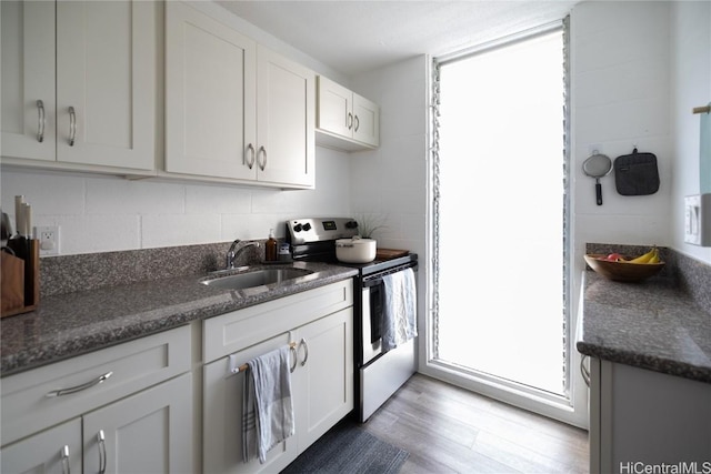 kitchen with dark stone counters, white cabinets, a sink, and electric range