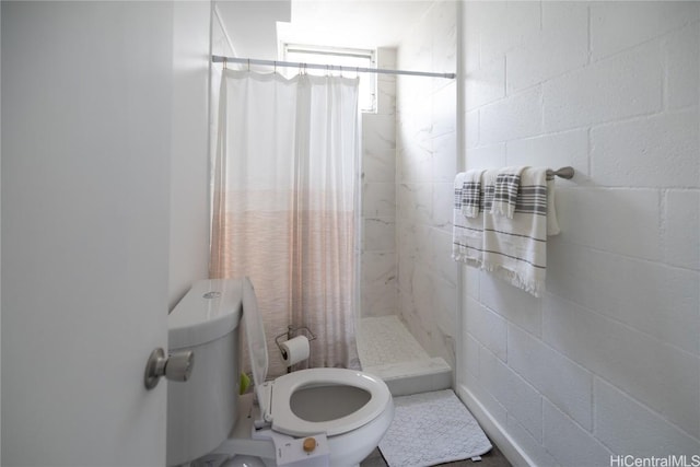 bathroom featuring a stall shower, concrete block wall, and toilet