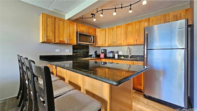 kitchen with light wood-style flooring, a breakfast bar, a peninsula, stainless steel appliances, and a sink