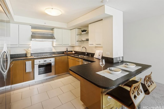 kitchen with a peninsula, under cabinet range hood, stainless steel oven, open shelves, and a sink