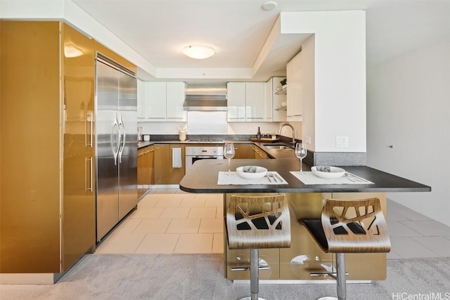 kitchen with white oven, built in refrigerator, dark countertops, and a sink