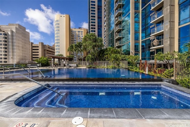 community pool featuring a view of city, fence, and a community hot tub