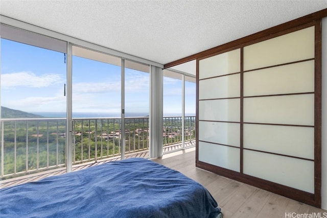 bedroom featuring light wood-style floors, floor to ceiling windows, and a textured ceiling