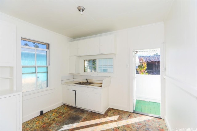 kitchen featuring a sink, baseboards, white cabinets, light countertops, and crown molding