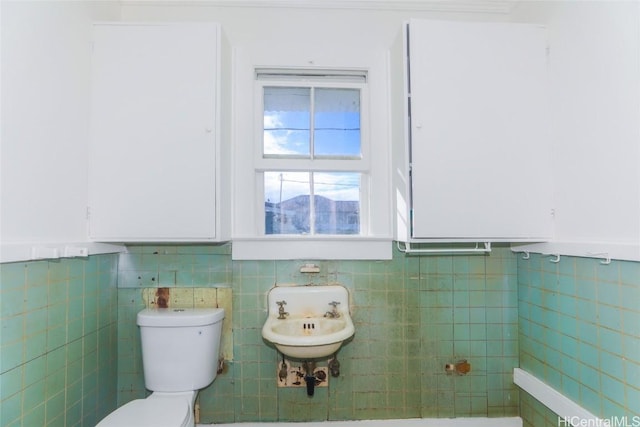 half bath with a sink, toilet, and tile walls