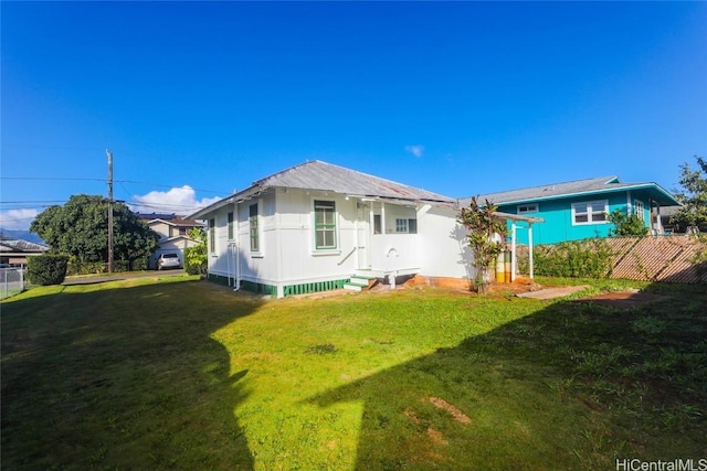 rear view of house with entry steps, fence, and a yard