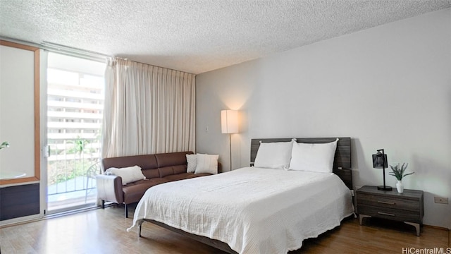 bedroom with a textured ceiling, floor to ceiling windows, wood finished floors, and access to exterior