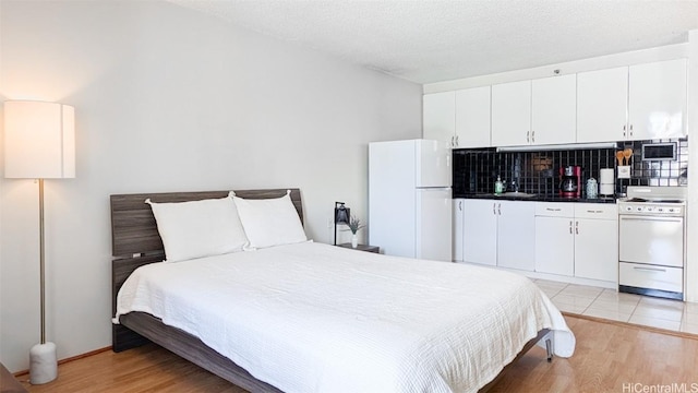 bedroom featuring freestanding refrigerator, light wood-style flooring, and a textured ceiling