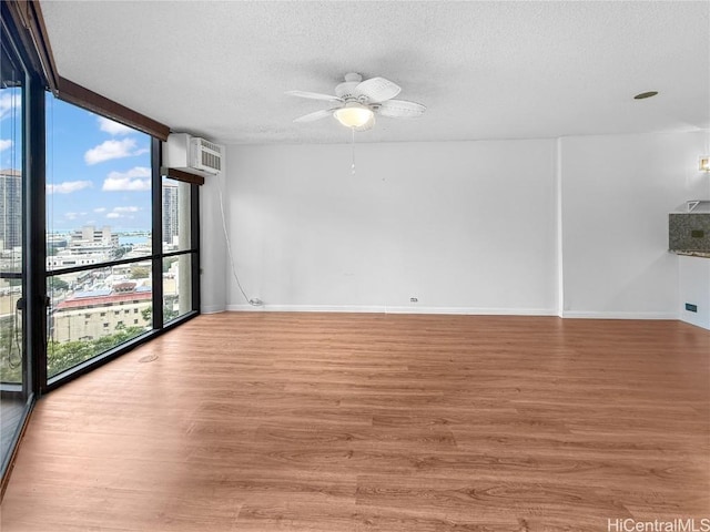 spare room featuring a textured ceiling, wood finished floors, baseboards, floor to ceiling windows, and a view of city